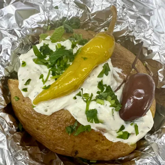 Folienkartoffel – Perfekt gegarte Kartoffel mit Knoblauchsauce, Kräutersauce oder Tzatziki, serviert auf einem Teller.