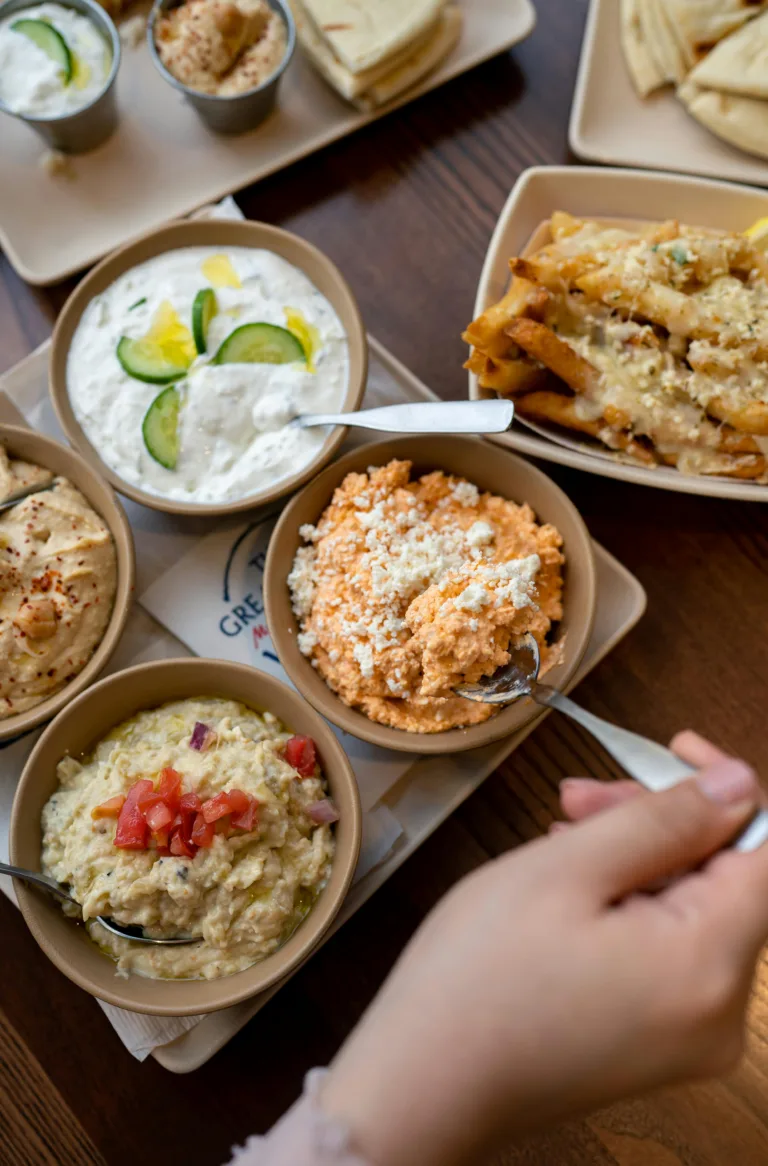 A vibrant assortment of Mediterranean dips and snacks, featuring colorful ingredients and hands serving food.