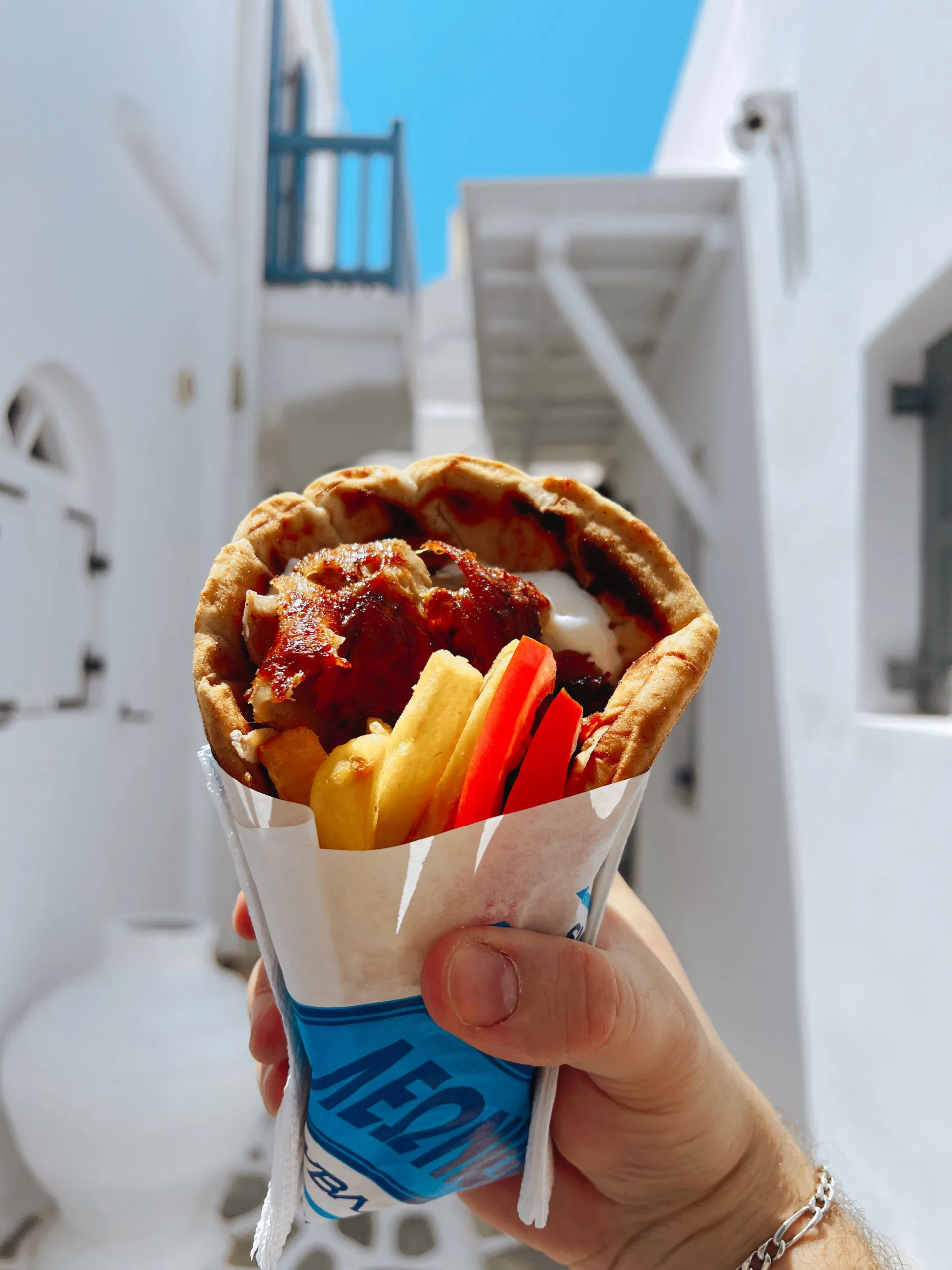 Close-up of a Greek gyro wrap held up against a bright Greek alleyway.