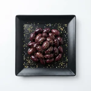 Schwarze Kalamata Oliven mit Olivenöl und Oregano auf schwarzem Teller vor weißem Hintergrund bei GyrosExpress Neukölln.